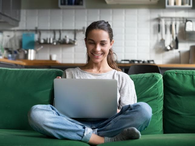 A woman sits on a sofa with a laptop
