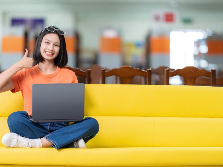 Student sitting on a sofa with her laptop with a thumbs up