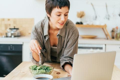 A woman logging onto her laptop while eating lunch 