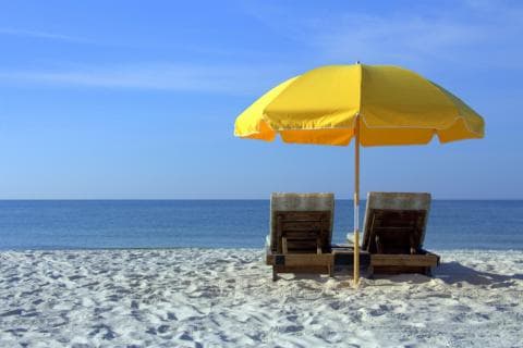 Two sun loungers sit on white sand, shaded by a yellow beach umbrella 