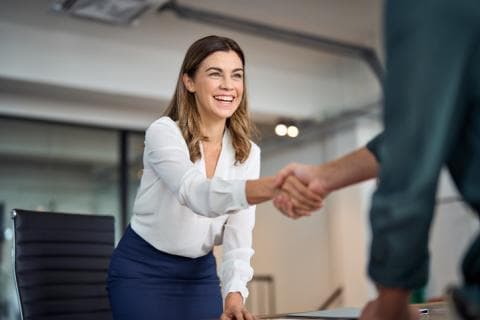 A woman shakes hand with a unseen person in an office setting