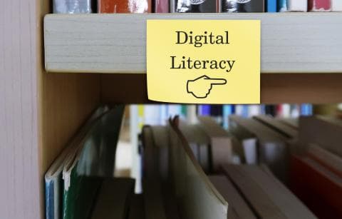 A sign saying "digital literacy" hung up on a shelf with books behind it