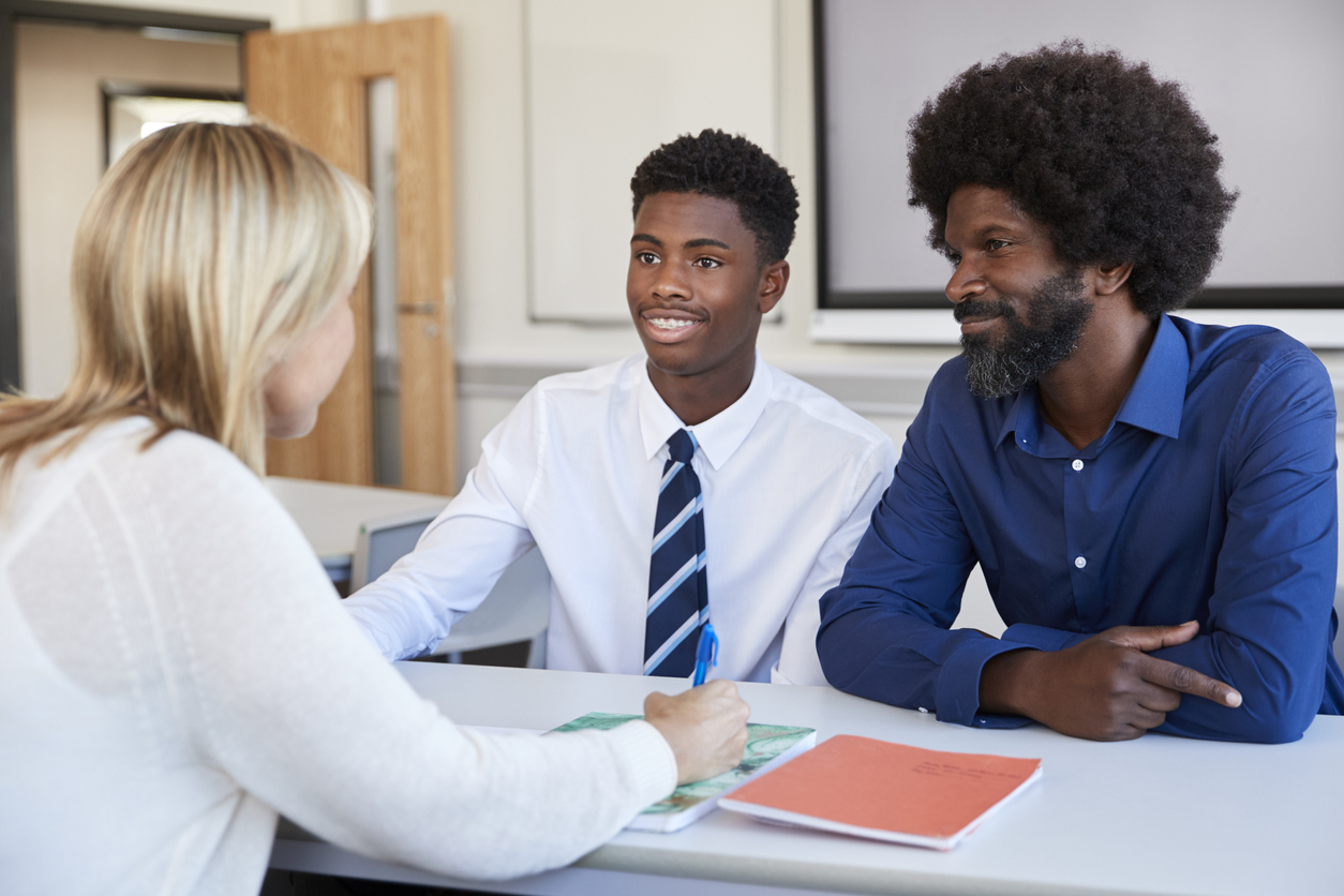 A boy and his father talk to a member of school staff