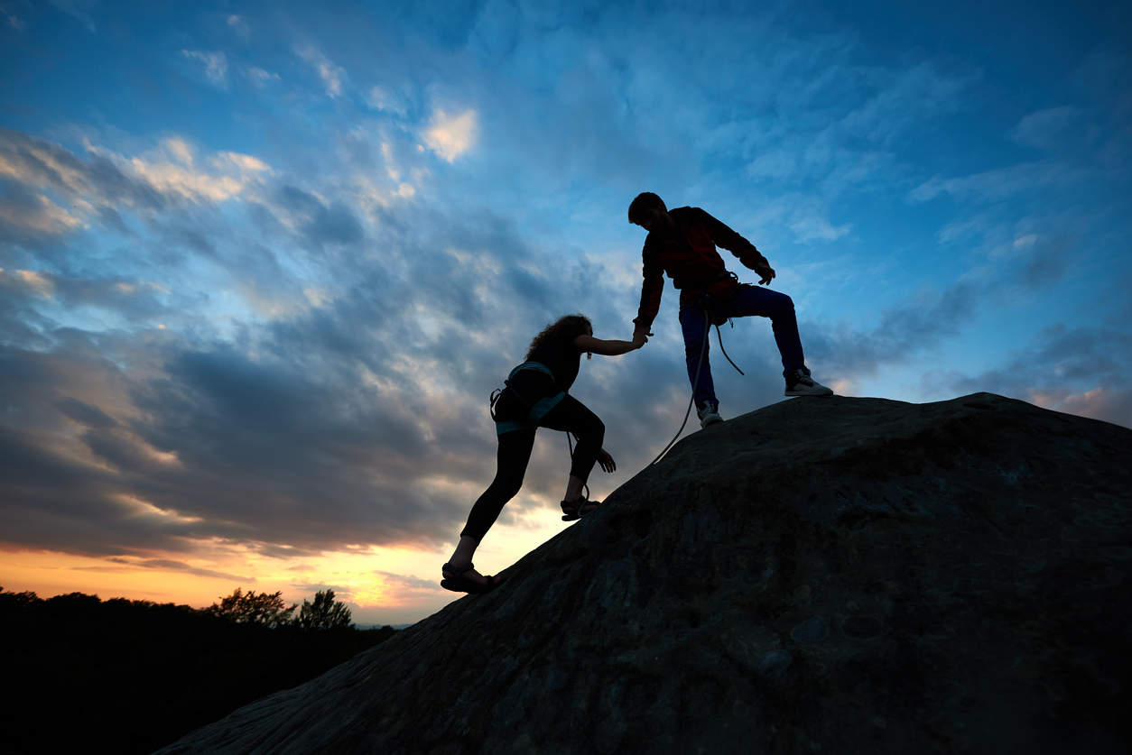 A mountaineer extends a hand to help a fellow climber to the summit