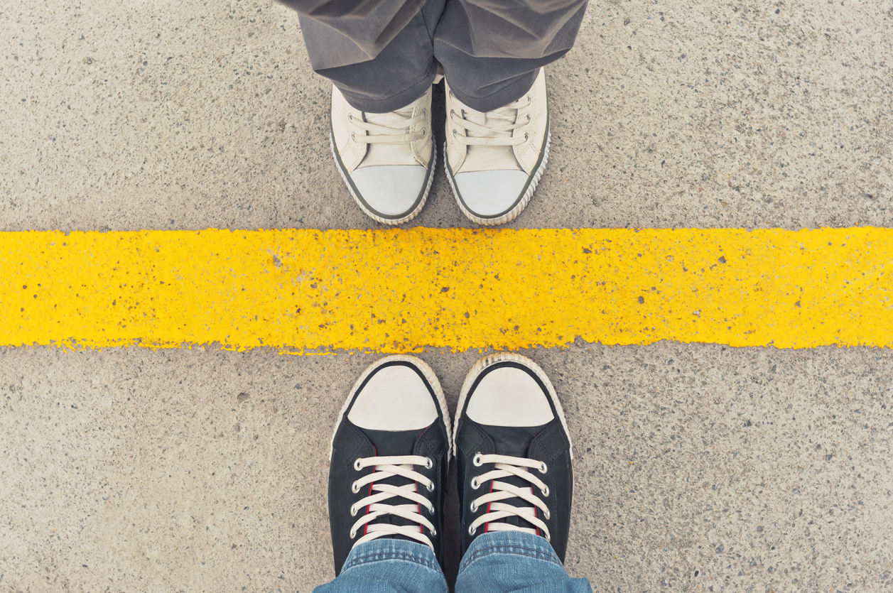 Two sets of feet, standing either side of a thick yellow line