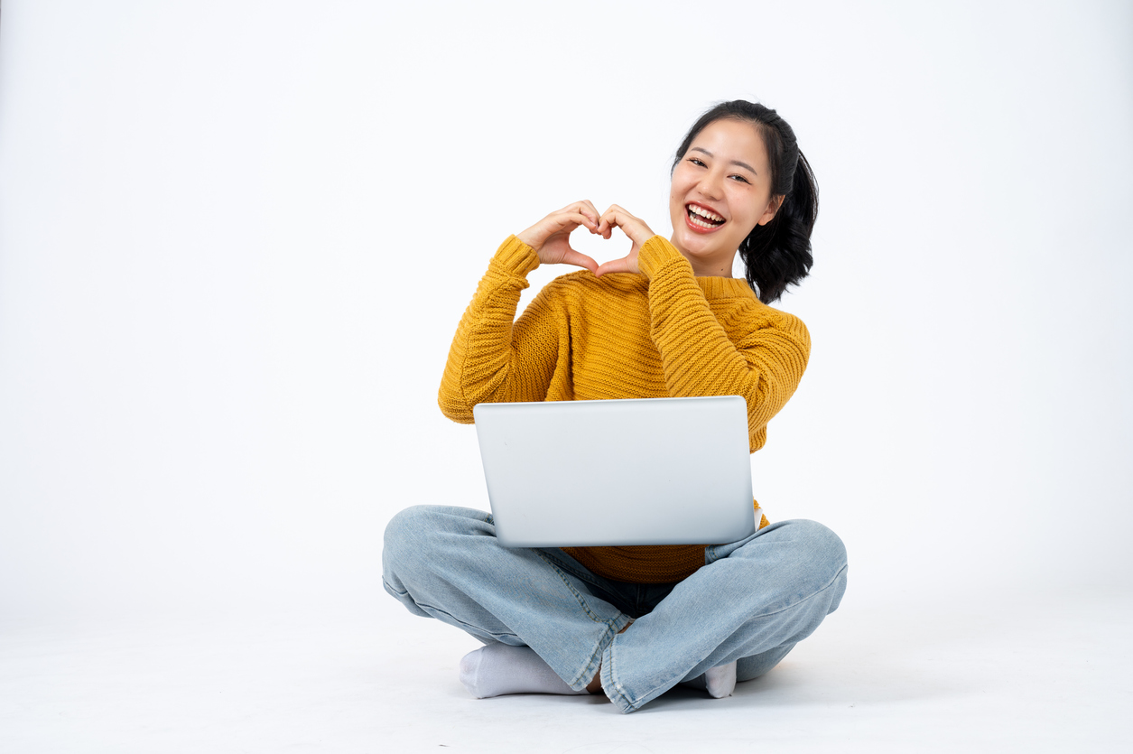 Happy woman sitting with laptop, making heart shape with hands