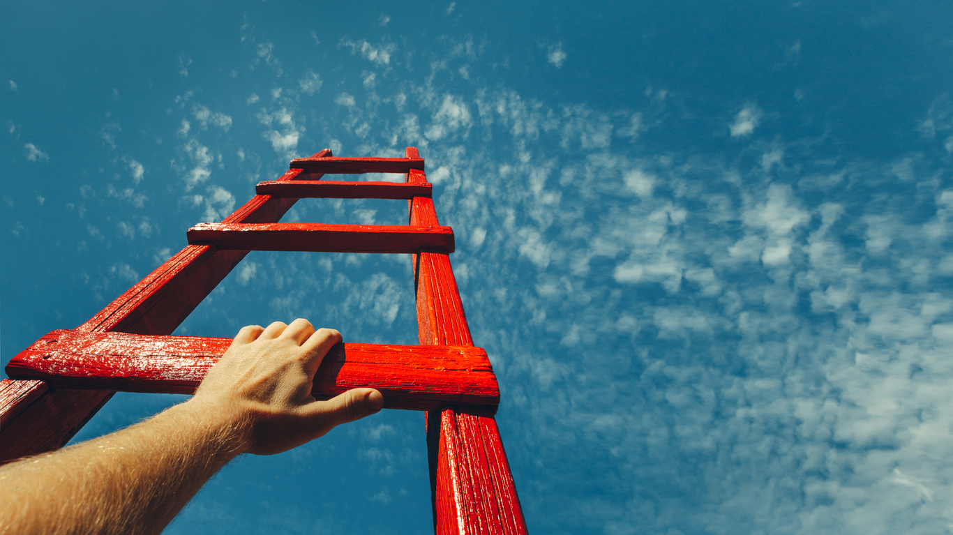 Hand on rung of ladder reaching up to the sky