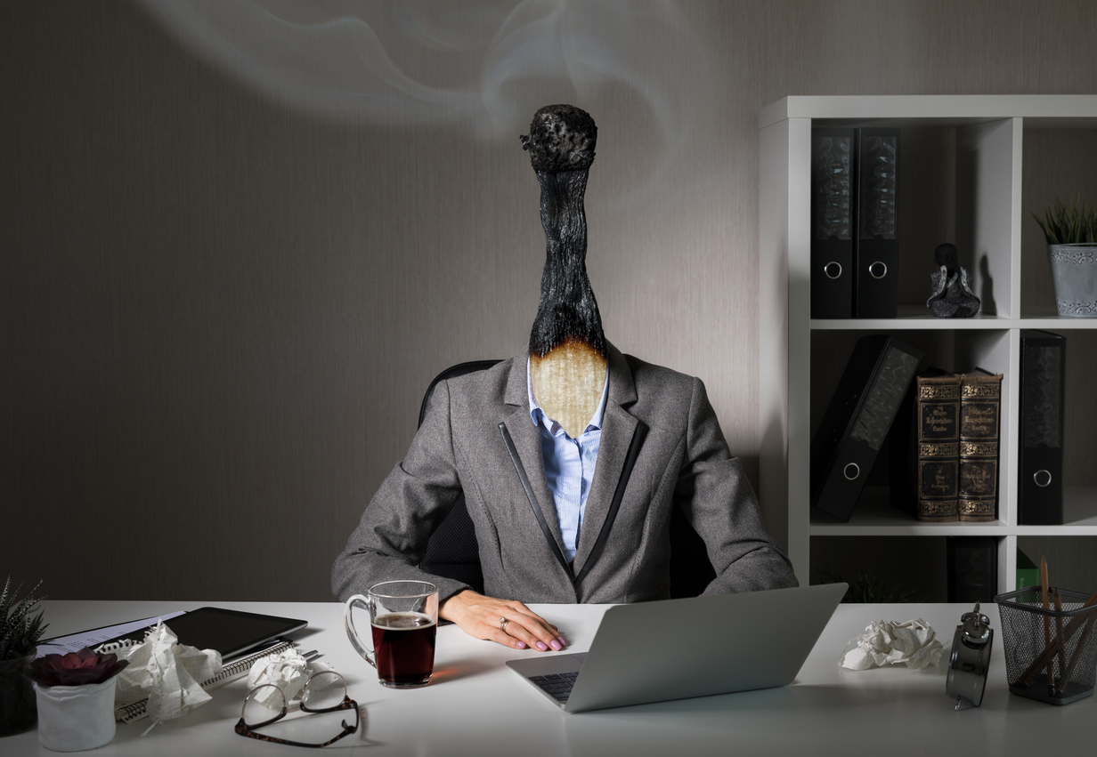 Woman sitting at her desk, with her head replaced by a burnt-out match