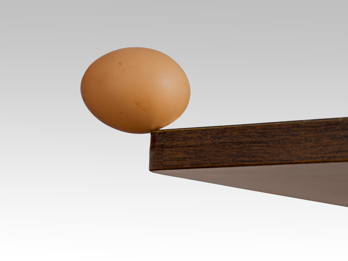 Egg, balanced precariously on the edge of a table