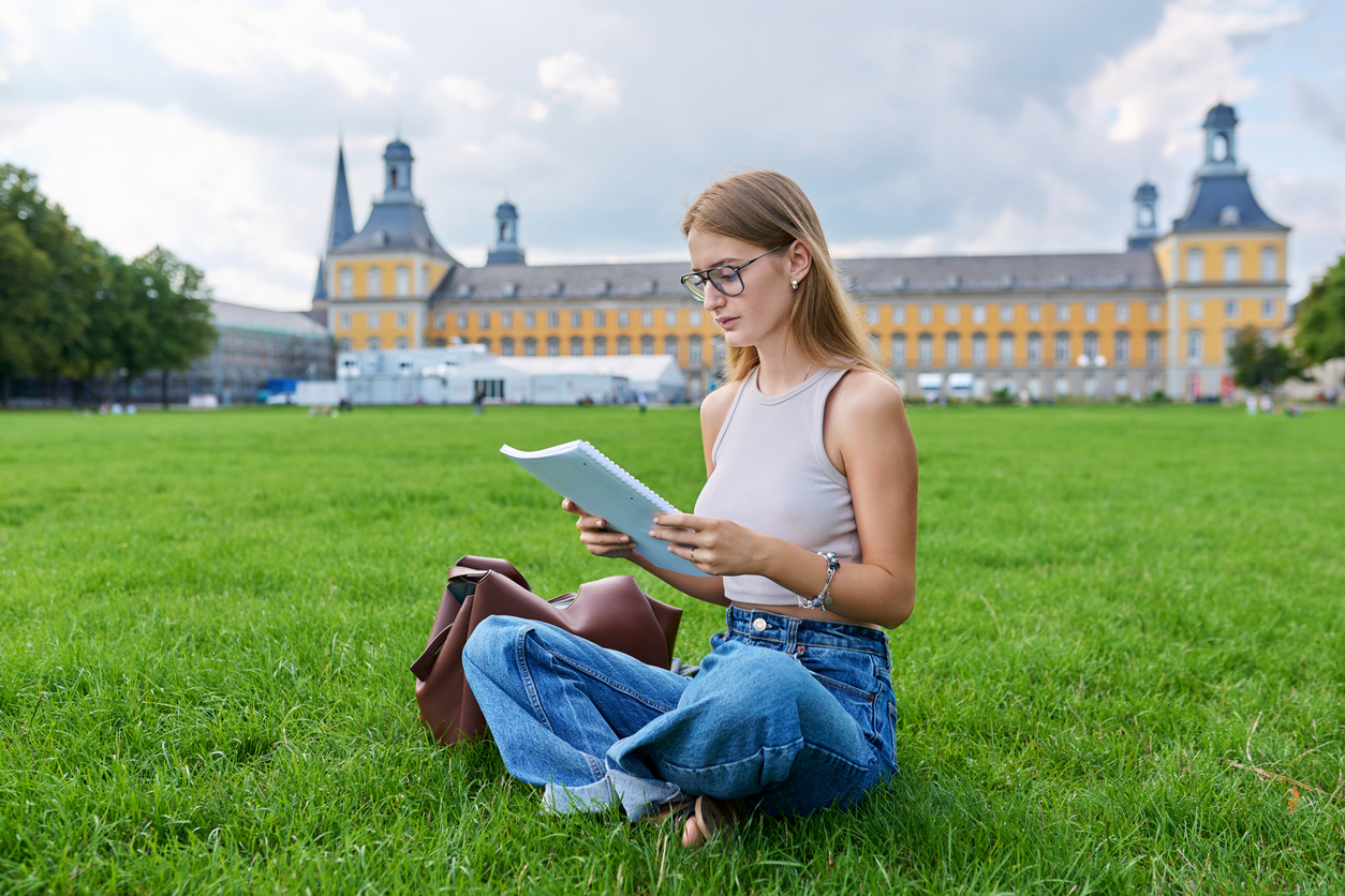 Student sitting on the lawn in front of Bonn University