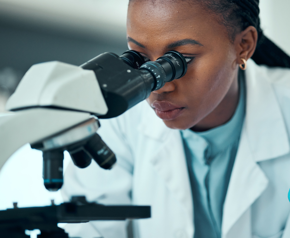 Woman in white coat, looking into microscope