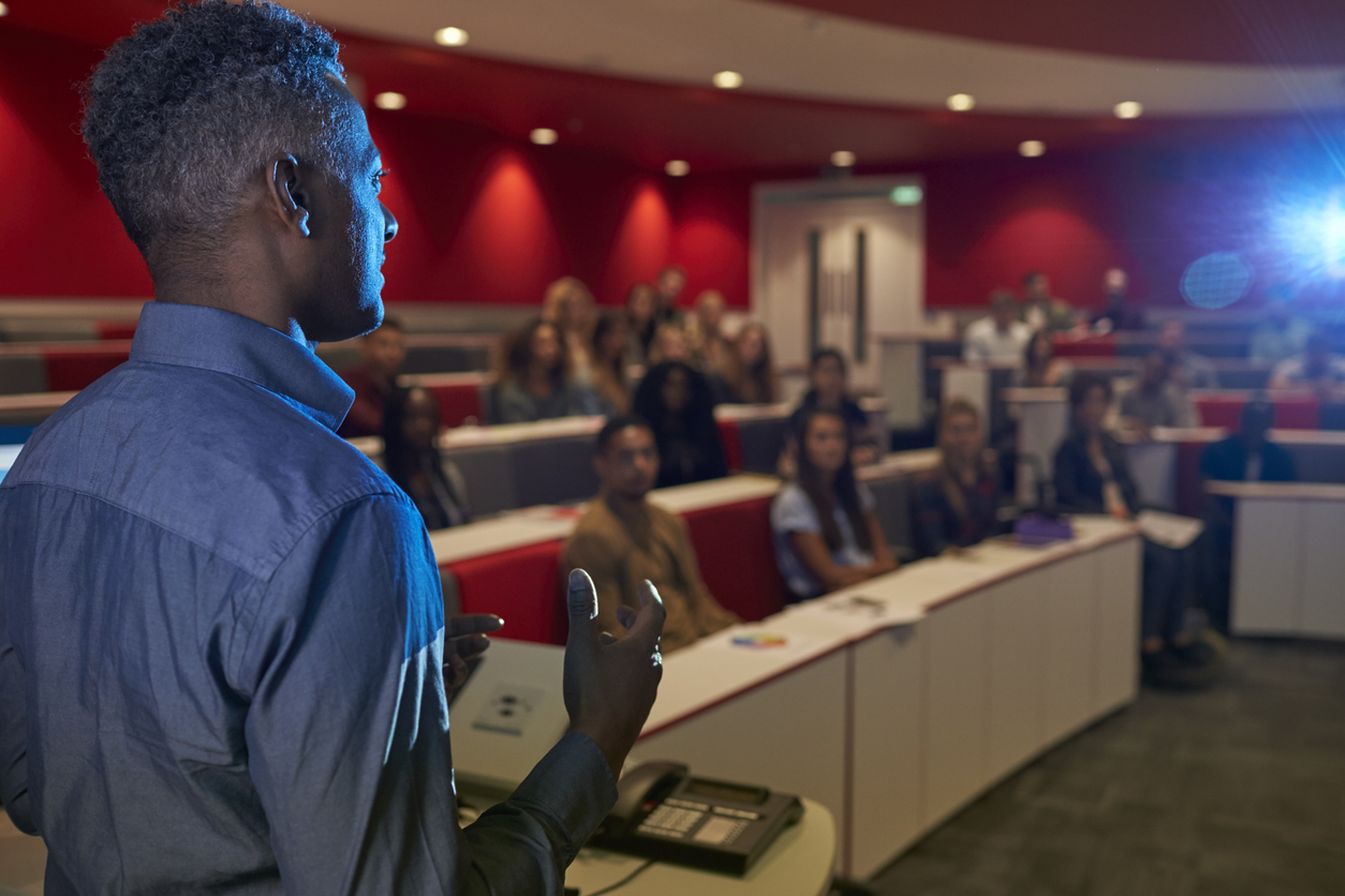 Man delivering a talk to lecture theatre full of students