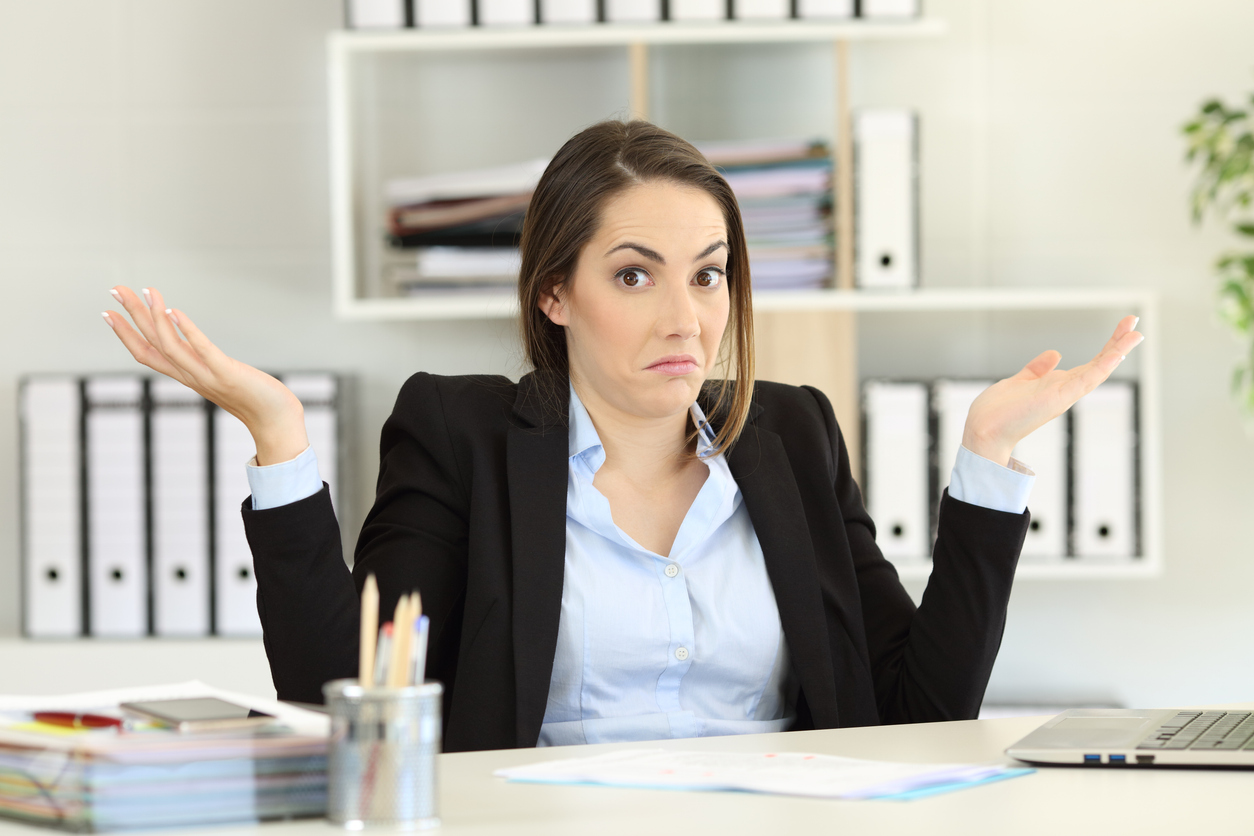 Woman at desk, shrugging and looking confused