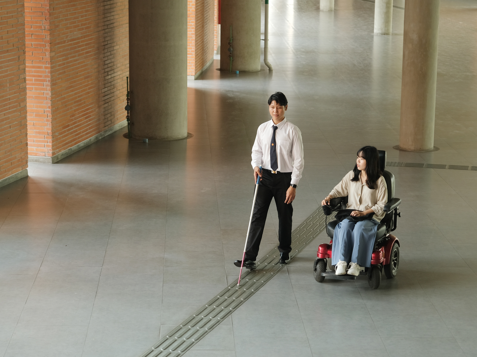 Person with a visual impairment walking next to person using a wheelchair