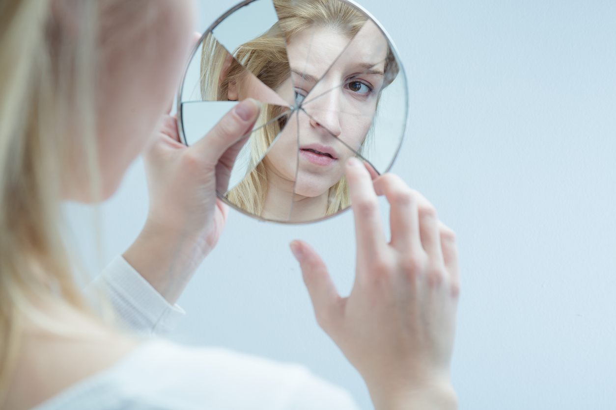 Woman looking in shattered mirror