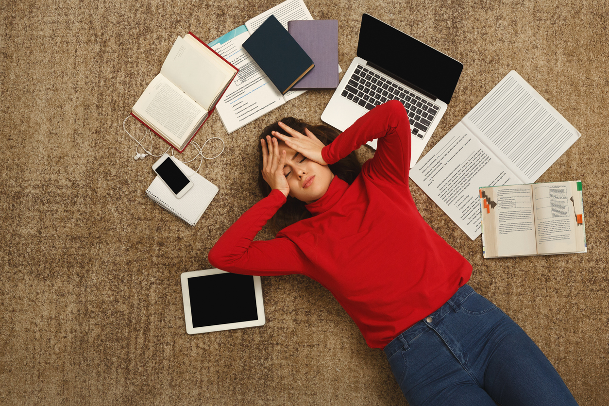 Student surrounded by study material, looking stressed