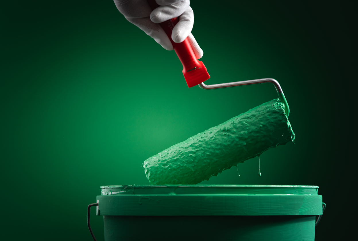 Paint roller dipped in pot of green paint