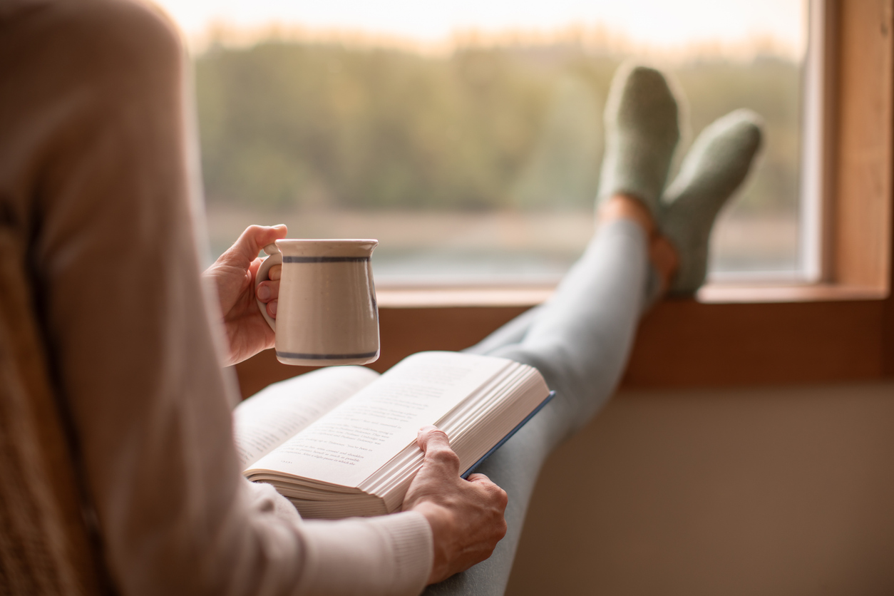 Woman drinking tea and reading, with feet up