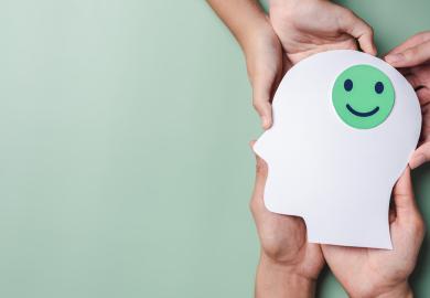 Hands holding a cut-out of a head, with a smiling face on it