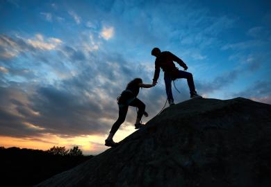 A mountaineer extends a hand to help a fellow climber to the summit