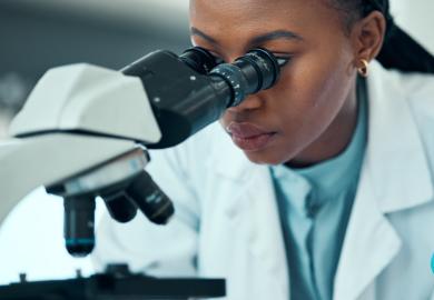 Woman in white coat, looking into microscope