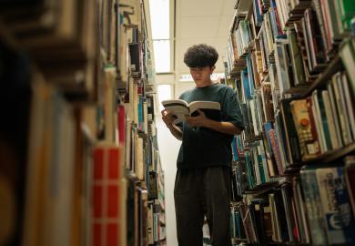 Student standing in library, reading