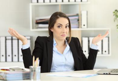 Woman at desk, shrugging and looking confused