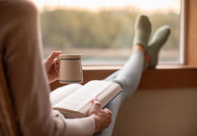 Woman drinking tea and reading, with feet up