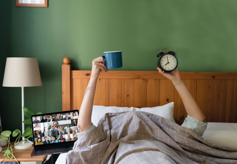 Montage of Hands of unrecognizable woman holding coffee and a clock while lying under the duvet in bed with a laptop next to her.jpg