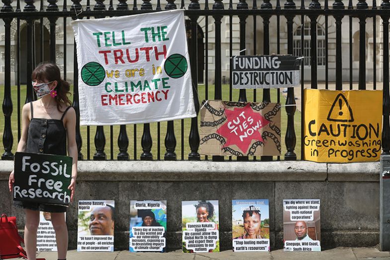 A climate change protester holds a sign saying 'Fossil Free Research' in front of the railings of the University's Senate House in Cambridge, England