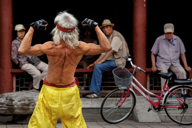 elderly Chinese man flexes his muscles as he performs a martial arts routine on the street, Beijing, China