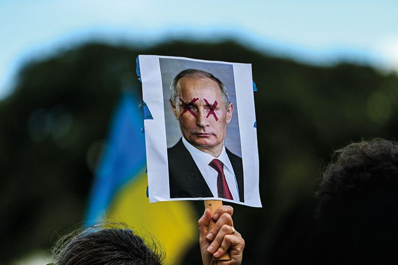 A demonstrator holds a sign depicting Russian President Vladimir Putin with eyes crossed out during a rally in support of Ukraine