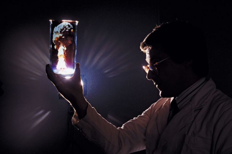 A scientist holds up a test tube in which we see a mushroom cloud, a symbolic image for nuclear cold fusion.