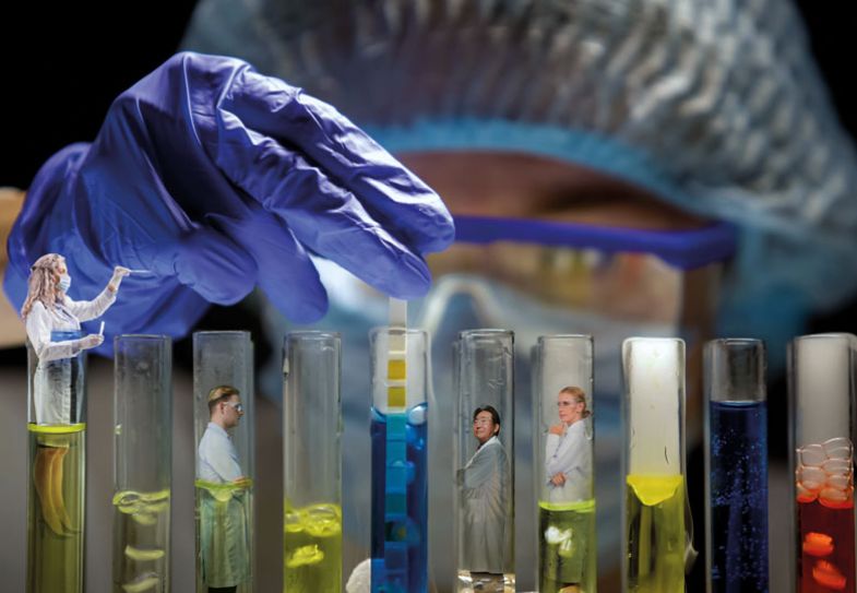 Scientist measuring acidity level in tube with blue liquid in dark laboratory with people inside each test tube