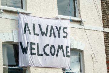 a banner hangs at the front of a London house with the caption 'Always Welcome'