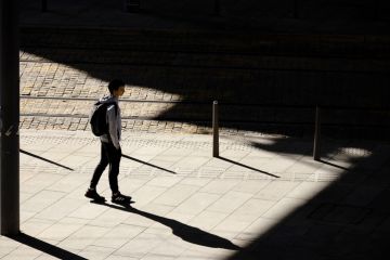 Belgrade, Serbia - October 26, 2020 One teenage boy standing alone waiting for a tram on bus stop in sunlight, high angle view from behind, with shadows