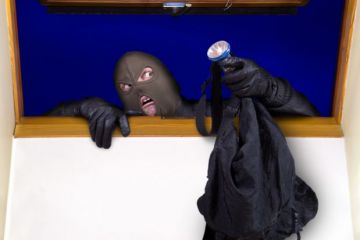 A masked person climbing through a window