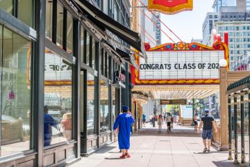 Chicago, IL  USA - May 24,2020 A young man in cap and gown walks under a sign downtown at the Chicago Theater, saying Congrats Class of 2020.