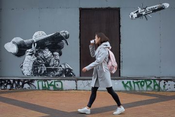 A woman passes by graffiti depicting a Ukrainian serviceman making a shot with a US-made Javelin portable anti-tank missile system in central Kyiv