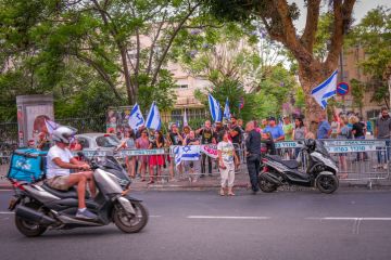 A small group of left-wing protesters stands on the side of the road in Tel Aviv, while police officer is guarding them.