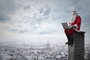 Santa sitting on a chimney with a laptop