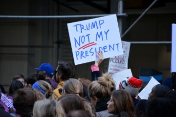 Someone in a crowd holds up a sign saying 'Trump - not my president'