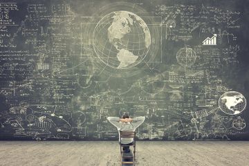 Man sitting on chair looking at blackboard full of scientific figures and graphs