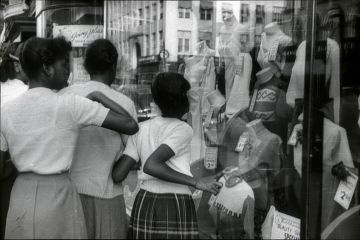 New York City, NYS, USA, 1951. Afro-American teenagers in front of a shop window in Harlem. They look at the offers of a fashion store.