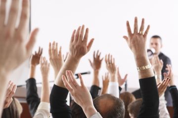People raise their hands in a meeting, illustrating no-confidence votes