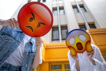 People holding the signs featuring different emoji faces. Too illustrate how neurodiverse and non-English speaking academics can be misunderstood