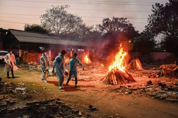 Workers carry the body of a person who has died of Covid-19 as funeral pyres burn during a mass cremation at a crematorium, New Delhi, 2021/05/03  