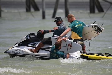 Mick Fanning of Australia (R) helps teammate Matt Wilkinson with his broken board during the qualifiers for the final of the WSL Founders' Cup of Surfing