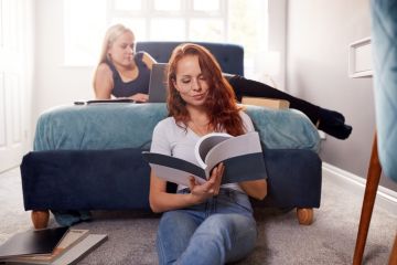 Two Female College Students In Shared House Bedroom Studying Together