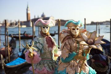 Venice, Veneto, Italy - February 19, 2020 Colourful and beautifully crafted costumes for this couple posing at San Marco square waterfront at sunset.
